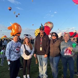Five people stand together on the grounds of the International Balloon Festival with colorful hot air balloons rising in the background